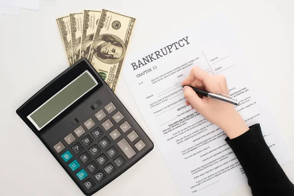 Vista recortada de la mujer llenando formulario de bancarrota con pluma cerca de dinero y calculadora sobre fondo blanco - foto de stock