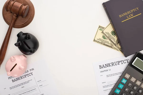 Top view of bankruptcy papers and law book, gavel, piggy banks, money and calculator on white background — Stock Photo