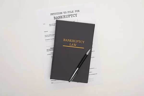 Vista superior del papel de bancarrota, el libro de leyes y la pluma sobre fondo blanco - foto de stock