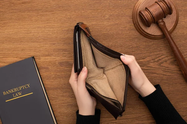 Vista superior de las manos femeninas con cartera vacía, libro de leyes de bancarrota y mazo sobre fondo de madera - foto de stock