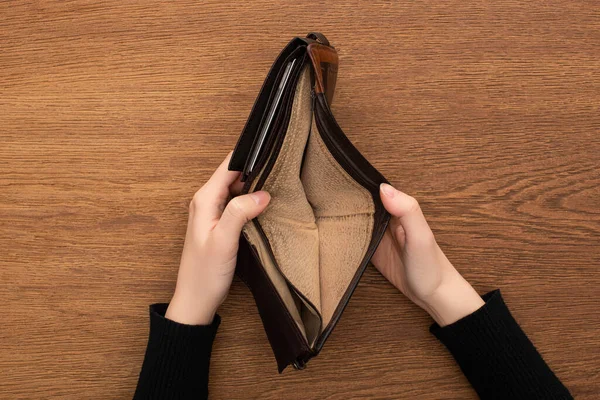 Top view of female hands with empty wallet on wooden background — Stock Photo