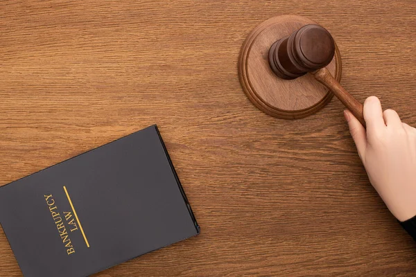 Vue recadrée de la main féminine avec marteau près de la faillite livre de loi sur fond en bois — Photo de stock