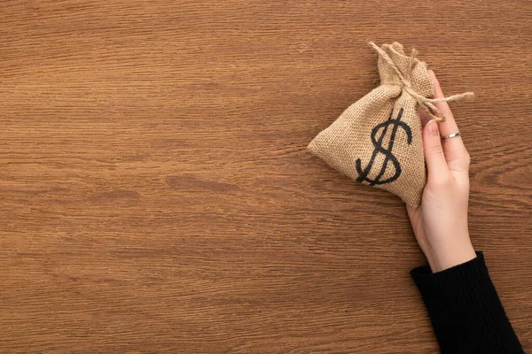 Cropped view of woman holding money bag on wooden background — Stock Photo