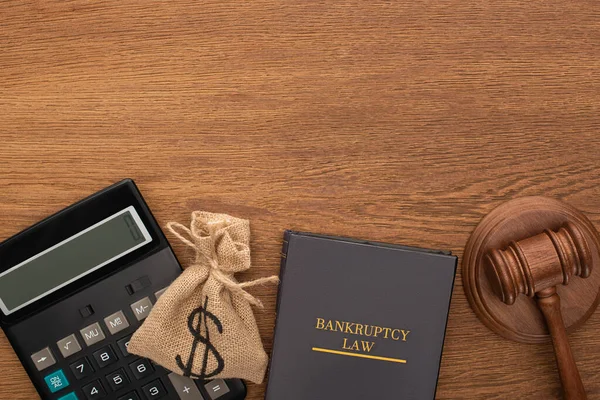 Vista superior del libro de leyes de bancarrota, bolsa de dinero, calculadora y martillo sobre fondo de madera - foto de stock