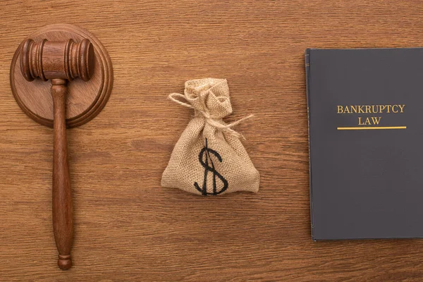 Верхний вид книги о банкротстве, сумка с деньгами и галстук на деревянном фоне — стоковое фото