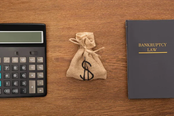 Vista superior del libro de leyes de bancarrota, bolsa de dinero, calculadora sobre fondo de madera - foto de stock