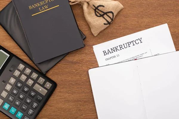 Vista superior del papel de bancarrota, libro de leyes, bolsa de dinero y calculadora sobre fondo de madera - foto de stock