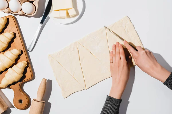 Zugeschnittene Ansicht einer Frau, die Teig für Croissants auf weißem Hintergrund schneidet — Stockfoto