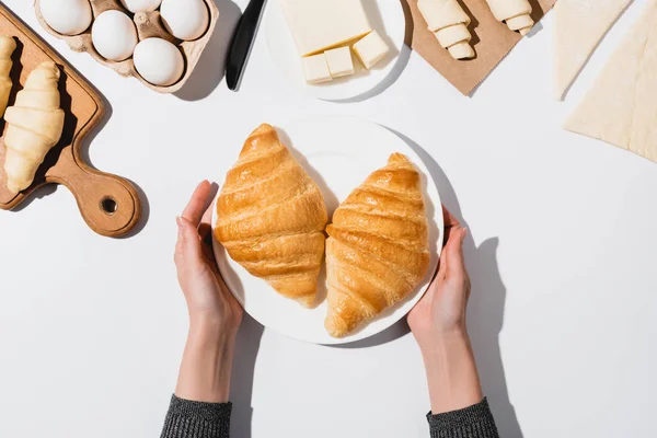 Vista ritagliata di donna che tiene piatto con croissant al forno su sfondo bianco — Foto stock