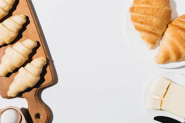 Vista superior de croissants cozidos no forno saboroso na placa perto cru na placa de corte no fundo branco — Fotografia de Stock