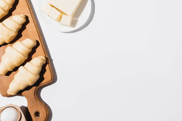 Vue de dessus des croissants crus frais sur planche à découper en bois près de beurre et oeuf sur fond blanc — Photo de stock