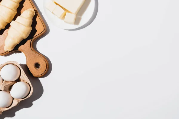 Vue de dessus des croissants crus frais sur planche à découper en bois près du beurre et des œufs sur fond blanc — Photo de stock