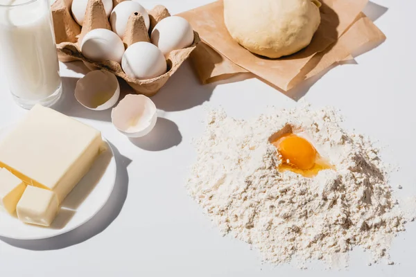 Fresh raw dough, flour, milk, butter and eggs on white background — Stock Photo