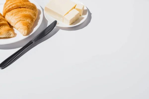 Croissants frescos sabrosos horneados en el plato cerca de la mantequilla con el cuchillo sobre fondo blanco - foto de stock