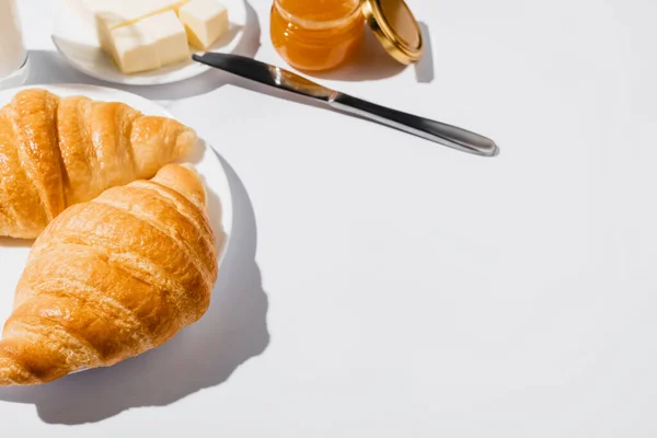 Leckere frisch gebackene Croissants auf Teller in der Nähe von Butter mit Messer und Marmelade auf weißem Hintergrund — Stockfoto