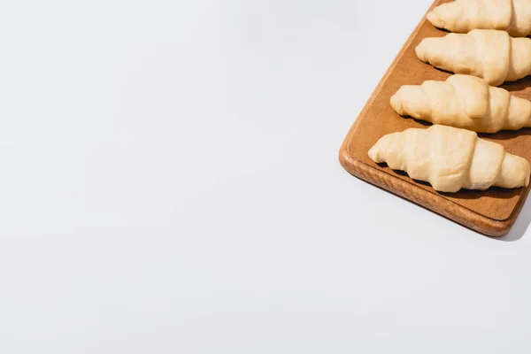 Frische rohe Croissants auf Holzschneidebrett auf weißem Hintergrund — Stockfoto