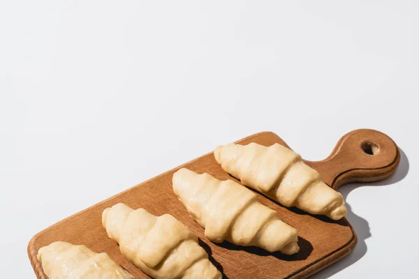 Croissant freschi grezzi su tagliere in legno su sfondo bianco con spazio per copiare — Foto stock