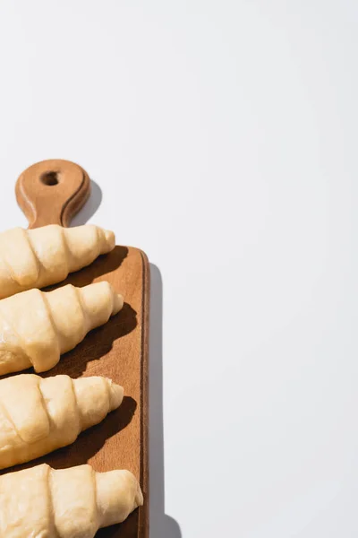 Croissant freschi grezzi su tagliere in legno su fondo bianco — Foto stock