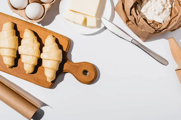 Top view of raw croissants on wooden cutting board near ingredients on white background — Stock Photo