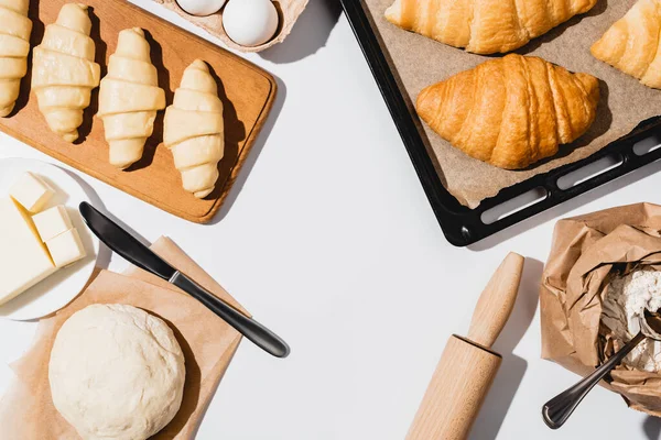 Vue de dessus des croissants crus et cuits sur plaque à pâtisserie près des ingrédients sur fond blanc — Photo de stock