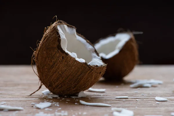 Selective focus of fresh tasty coconut halves and flakes on wooden table isolated on black — Stock Photo