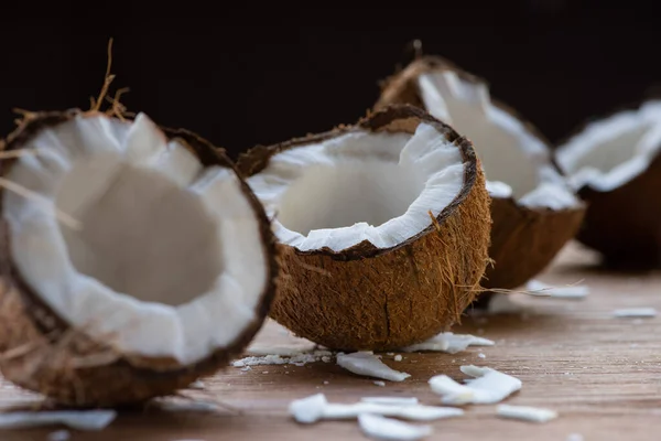 Selective focus of fresh tasty coconut halves and flakes on wooden table isolated on black — Stock Photo