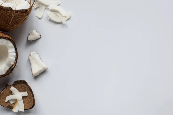 Draufsicht auf frische leckere Kokosnusshälften mit rissiger Schale und Flocken auf weißem Hintergrund — Stockfoto