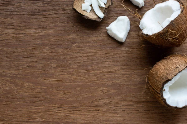 Blick von oben auf frisch geknackte Kokosnuss mit Flocken auf Holztisch — Stockfoto