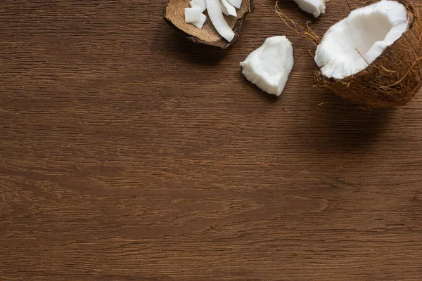Blick von oben auf frisch geknackte Kokosnuss mit Flocken auf Holztisch — Stockfoto