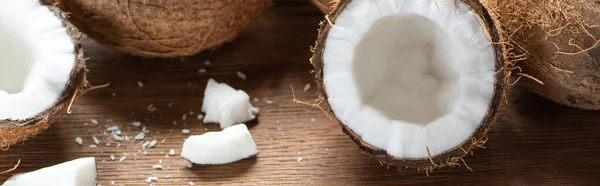 Fresh tasty whole and cracked coconuts and flakes on wooden table, panoramic shot — Stock Photo