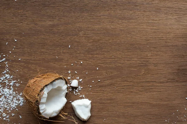 Vue de dessus de noix de coco fraîche savoureuse moitié près de flocons sur table en bois — Photo de stock