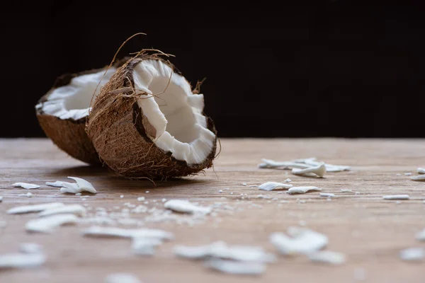 Foco seletivo de metades de coco saborosas frescas e flocos na mesa de madeira isolada em preto — Fotografia de Stock