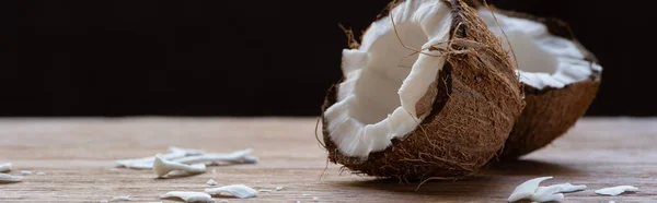 Foco seletivo de metades de coco saborosas frescas e flocos na mesa de madeira isolada em preto, tiro panorâmico — Fotografia de Stock