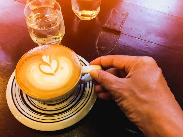Cappuccino och vatten på bordet med glas vatten och hand — Stockfoto