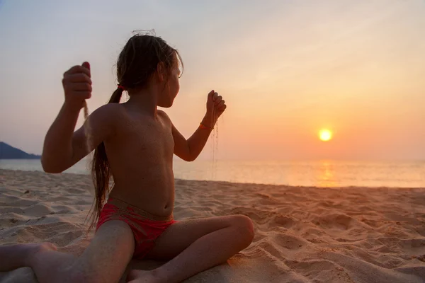 Dziewczynka bawi się piasku i wygląda o zachodzie słońca — Zdjęcie stockowe
