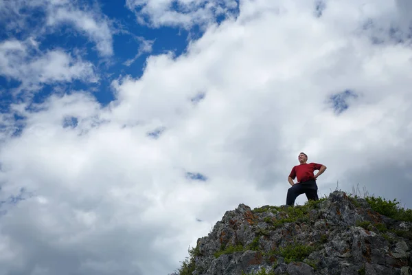 Un hombre en la cima de una montaña contra un cielo azul con nubes . — Foto de Stock