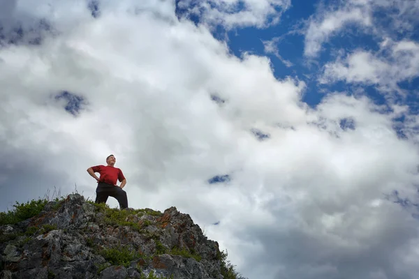 Un hombre en la cima de una montaña contra un cielo azul con nubes . — Foto de Stock