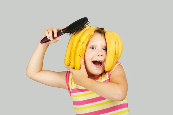 Kleine vrolijke meisje speelt met een banaan-kapsel — Stockfoto