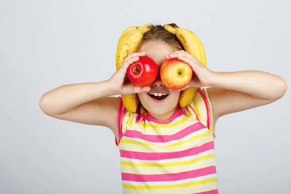 Веселая маленькая девочка с яблоками, лимоном и бананом позирует положительно — стоковое фото