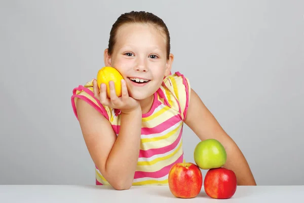 Niña alegre con manzanas y limón posa positivamente en s —  Fotos de Stock