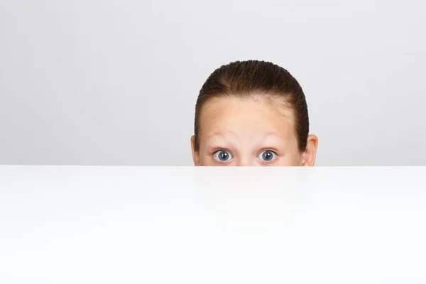 A little girl with fear in her eyes is hiding under the table. — Stock Photo, Image