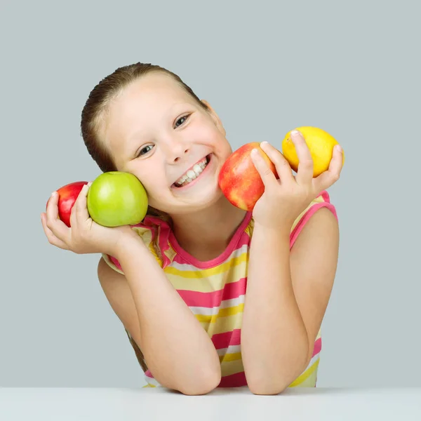 Fröhliches kleines Mädchen mit Äpfeln und Zitrone posiert positiv in s — Stockfoto