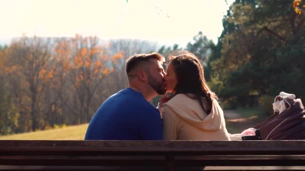 Jovem casal beijos em um banco de parque — Vídeo de Stock