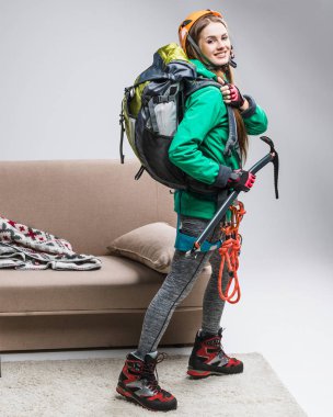 young happy climber with backpack, ice axe and climbing rope at home clipart