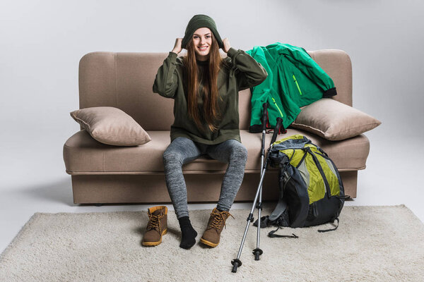 happy traveler wearing hat and hiking boots on sofa with backpack