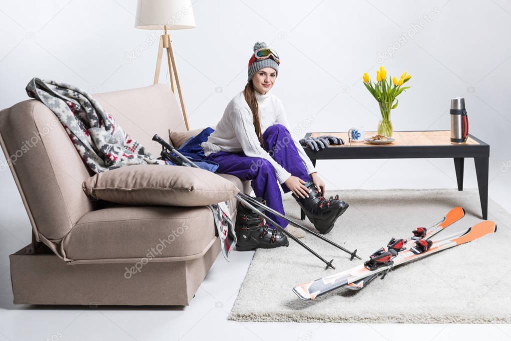 young female skier wearing ski boots while sitting on sofa at home