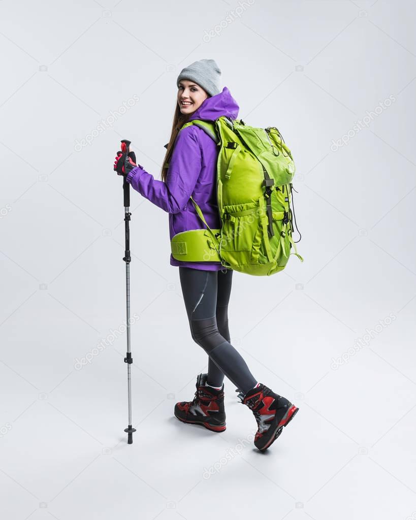 female hiker in warm clothing with backpack and hiking equipment, isolated on grey