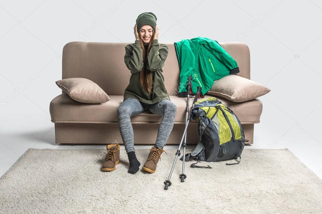 smiling girl wearing warm clothing and hiking boots on sofa with backpack
