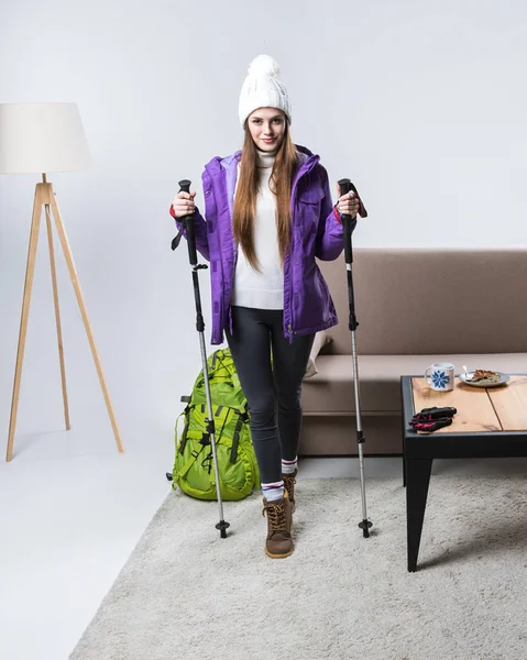 Belle sportive en vêtements chauds avec sac à dos et bâtons de randonnée à la maison — Photo de stock
