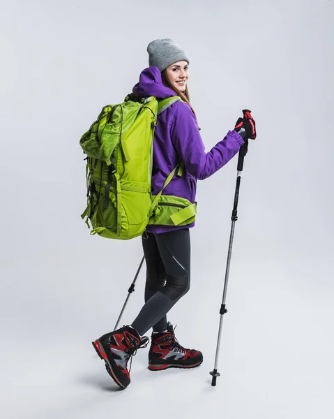 Giovane escursionista in abbigliamento sportivo con zaino e bastoni da trekking, isolato su grigio — Foto stock